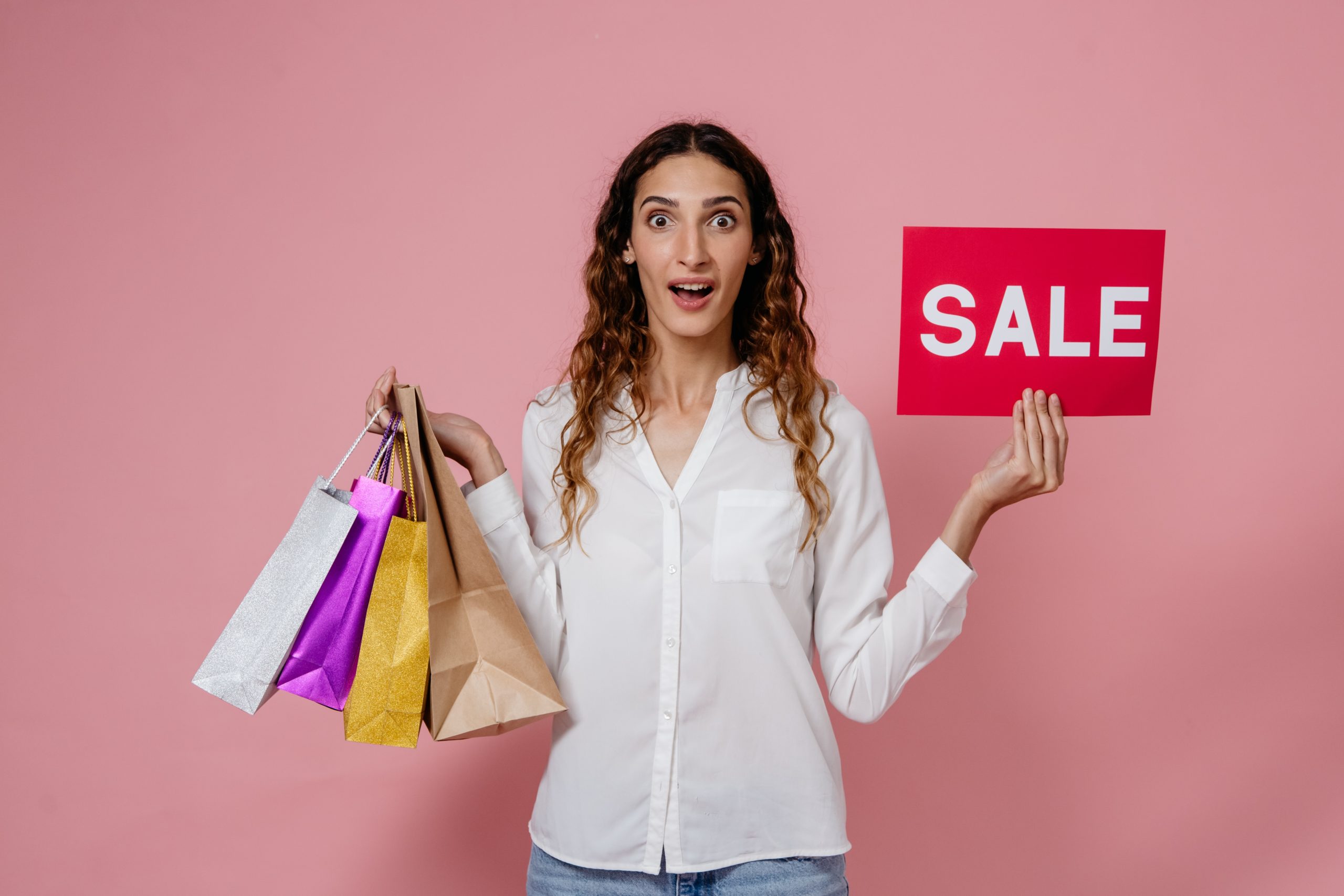 Woman holding 4 shopping bags and Sale sign with surprised look