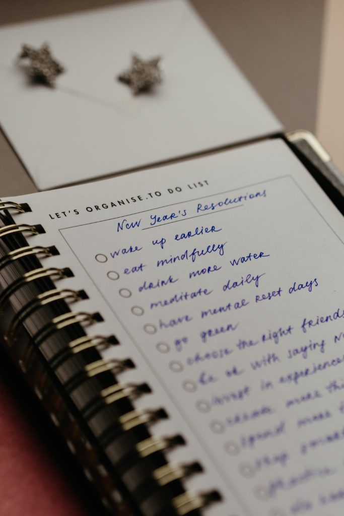 Photo of a notebook with New Year's Resolutions at the top.  Items in list below include "wake up earlier", "eat mindfully", "drink more water", "meditate daily", "have mental rest days", "go green".  